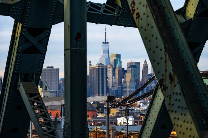 A view of the lower Manhattan skyline through the steel beams of a bridge.
